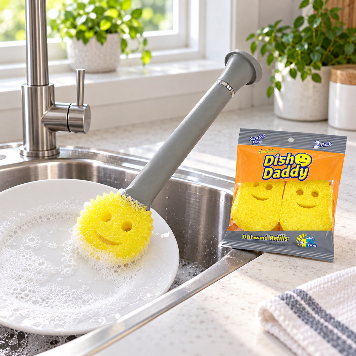 Dish Daddy soap-dispensing dishwand cleaning a plate beside the sealed two-pack of refill heads